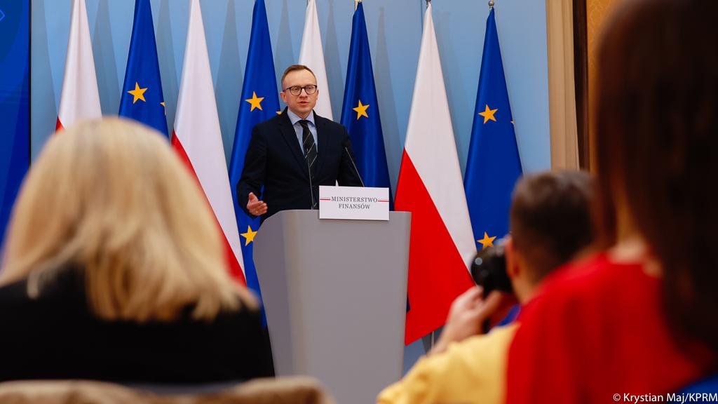 Wiceminister Finansów Artur Soboń przemawia na tle flag Polski i Uni Europejskiej