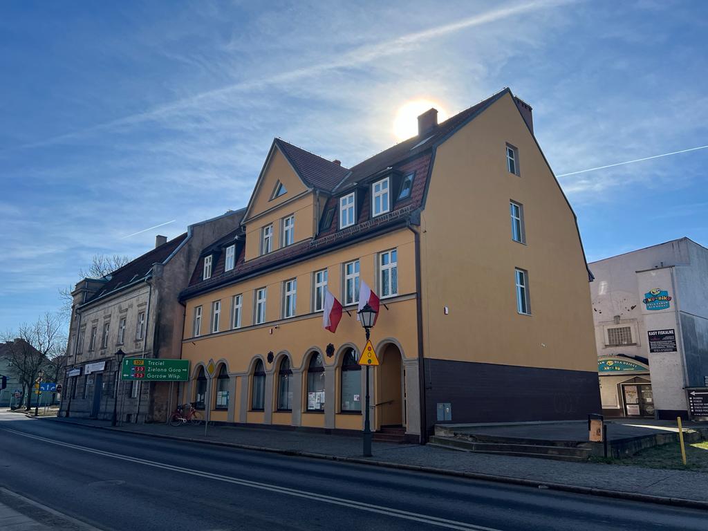 dzień, siedziba urzedu skarbowego, budynek w stylu kamienicy, w kolorze ciemno żółtym, budynek przy drodze, na budynku wizą dwie flagi Polski