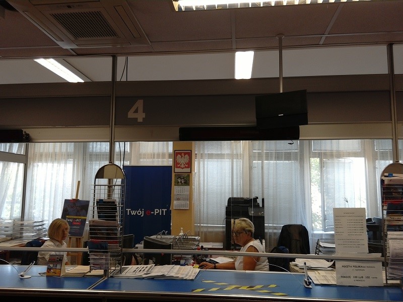 Wnętrze urzędu, sala podzielona na stanowiska obsługi, dwie urzędniczki siedzą na swich stanowiskach 