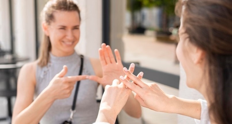 Dwie uśmiechnięte młode kobiety rozmawiają ze sobą w języku migowym