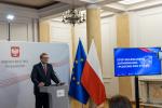 Mężczyzna w okularach stoi przy mównicy, obok flagi Polski Unii Europejskiej.