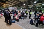 na dworcu dużo ludzi z Ukrainy z bagażami, 2 funkcjonariuszy służby celno-skarbowej stoi wśród nich