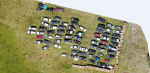 widok z lotu ptaka, na pustym zielonym terenie stoi zaparkowanych kilkadziesiąt aut