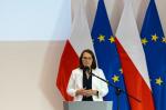 Minister Finansów Magdalena Rzeczkowska stoi na tle polskiej flagi i flagi Unii Europejskiej
