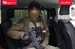 Funkcjonariusz Służby Celno-Skarbowej z grupy zadaniowej siedzi z bronią w busie. Na górze logo KAS
