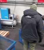 Funkcjonariusz Służby Celno-Skarbowej stoi w hali produkcyjnej koło niebieskiego metalowego pojemnika.