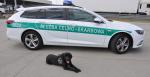 Pies Carlos (czarny labrador) leży koło auta służbowego Służby Celno-Skarbowej