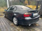 Czarne BMW 318 nadwozie typu sedan, ujęcie lewego tyłu, felgi stalowe z plastikowymi kołpakami w kolorze srebrnym, lusterka w kolorze nadwozia, przyciemniane tylne szyby, wgnieciony i zarysowany błotnik przedni lewy, wgniecione i zarysowane drzwi przednie lewe, antena radiowa typu „płetwa rekina