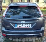 Tył granatowego samochodu Ford Fokus. W zderzaku brak zaślepki haka holowniczego oraz światła odblaskowego po prawej stronie.