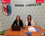 przy biurku siedzą dwie panie, za nimi ścianka z logo gminy Lubiszyn