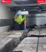 środek busa wypełnionego kartonami z nielegalnymi papierosami, funkcjonariuszka SCS pokazuje jedną sztangę nielegalnych papierosów