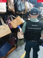 funkcjonariusz SCS stoi przy stanowisku na bazarze z podrabianym torebkami znanych firm