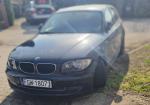 przód  czarnego BMW 116i z widocznym wyblakłym lakierem, wieloma zarysowaniami oraz uszkodzonym zderzakiem i połamanymi reflektorami